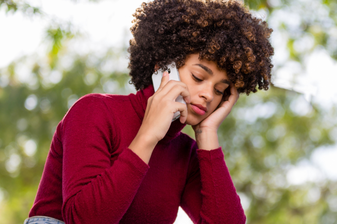 Woman sitting outside, looking slightly distressed holding a cell-phone to her ear.