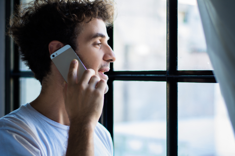 A young man holds his phone up to his ear to speak to a Mosaic Counseling intake specialist to set an appointment and get connected to therapy.
